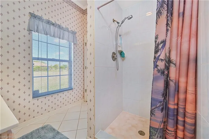 Bathroom featuring baseboards, tile patterned flooring, wallpapered walls, and tiled shower