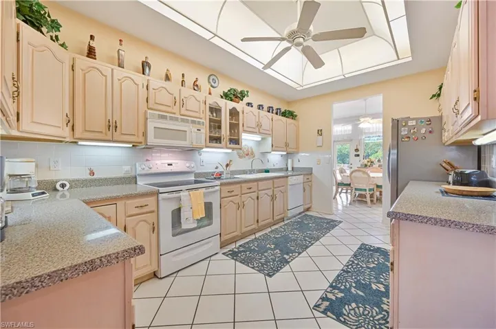 Kitchen featuring a sink, light tile patterned flooring, tasteful backsplash, white appliances, and ceiling fan