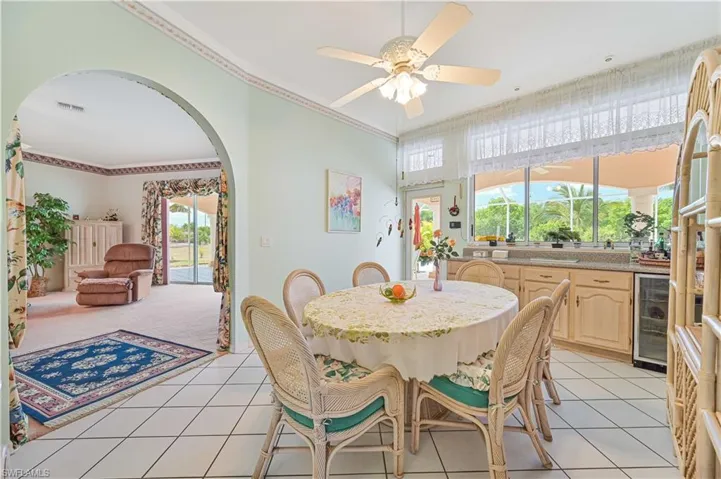 Dining area with wine cooler, arched walkways, light tile patterned floors, visible vents, and ornamental molding