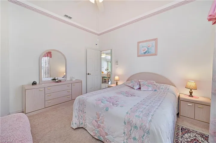 Bedroom featuring visible vents, a high ceiling, ceiling fan, crown molding, and carpet floors