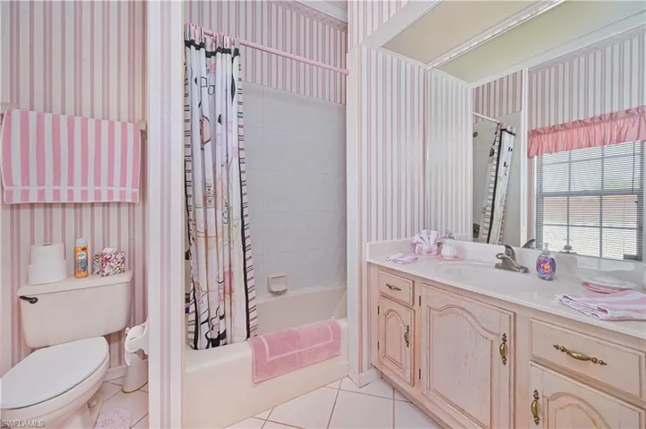 Bathroom featuring wallpapered walls, tile patterned flooring, shower / bath combination with curtain, toilet, and vanity
