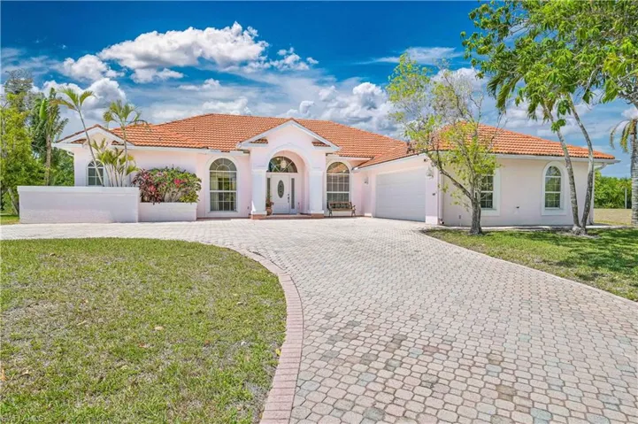 Mediterranean / spanish home with a front lawn, stucco siding, an attached garage, a tile roof, and decorative driveway