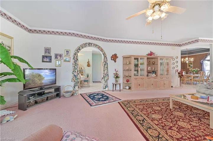 Carpeted living room featuring ceiling fan with notable chandelier, arched walkways, and crown molding