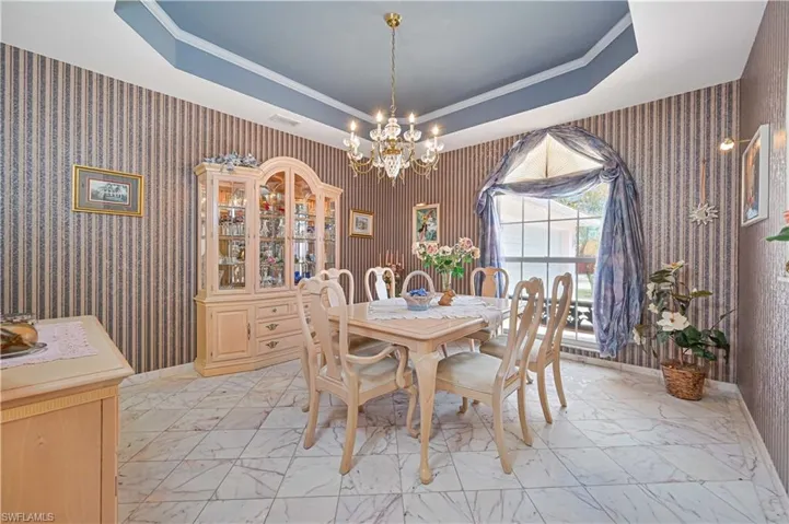 Dining area featuring wallpapered walls, marble finish floor, a notable chandelier, and a tray ceiling