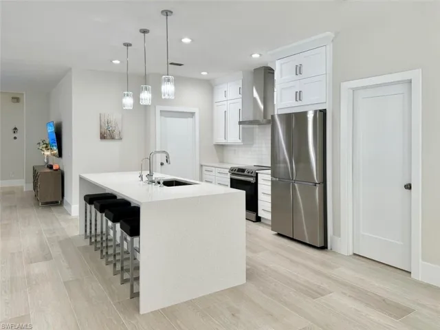 Kitchen with appliances with stainless steel finishes, wall chimney exhaust hood, white cabinets, light wood-style flooring, and light stone counters