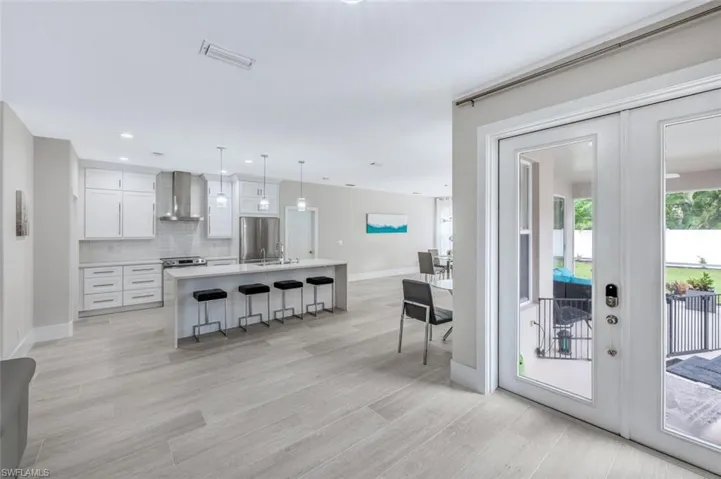 Kitchen with white cabinets, a kitchen breakfast bar, decorative light fixtures, wall chimney range hood, and stainless steel refrigerator