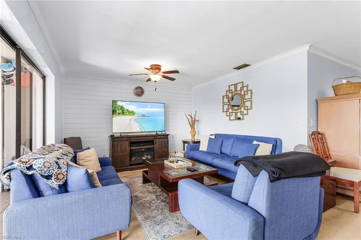 Living room featuring ornamental molding, wood walls, light wood-style flooring, a glass covered fireplace, and a ceiling fan