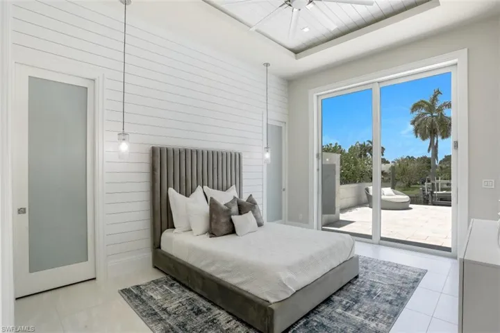 Bedroom with access to outside, a raised ceiling, wooden walls, and tile patterned floors