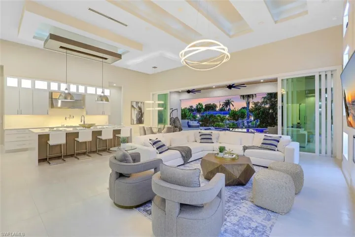 Living area with a towering ceiling, ceiling fan, light tile patterned flooring, beam ceiling, and a chandelier