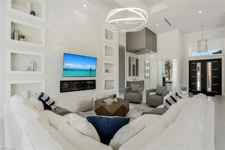 Living area featuring high vaulted ceiling, a chandelier, built in features, recessed lighting, and a glass covered fireplace