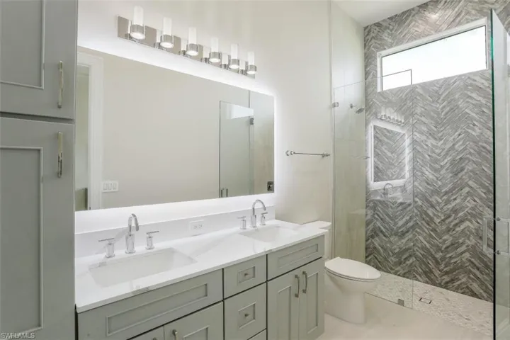 Bathroom with double vanity, toilet, and a stall shower