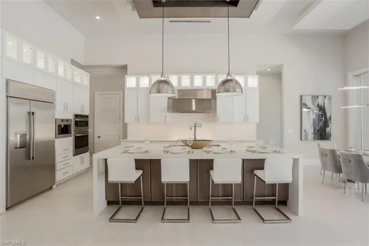 Kitchen featuring stainless steel appliances, wall chimney range hood, white cabinetry, light countertops, and a large island with sink