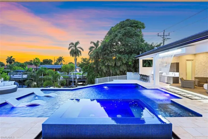 Pool at dusk featuring an in-ground hot tub, an outdoor pool, a patio area, and exterior kitchen