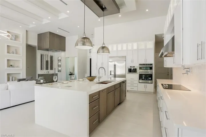 Kitchen featuring stainless steel appliances, a sink, wall chimney range hood, a high ceiling, and white cabinetry