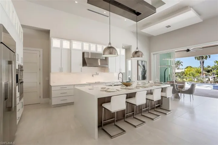 Kitchen featuring wall chimney exhaust hood, a sink, a high ceiling, backsplash, and stainless steel appliances