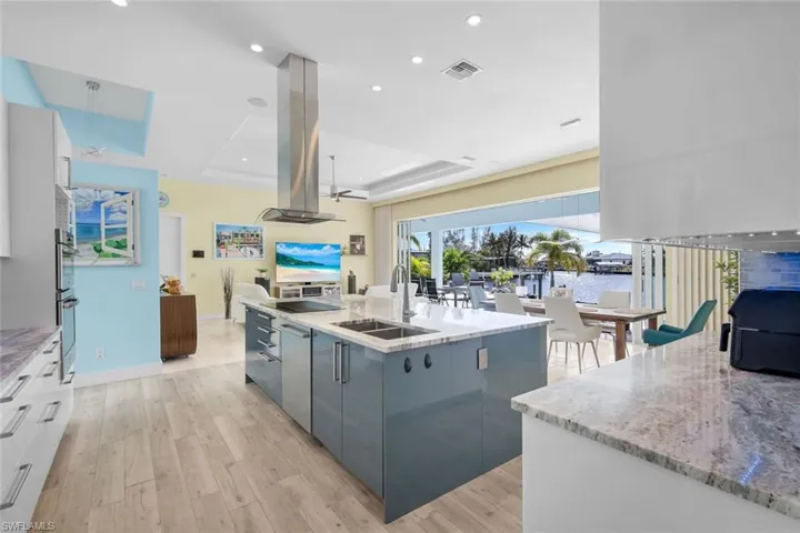 Kitchen featuring light stone counters, an island with sink, a tray ceiling, modern cabinets, and open floor plan