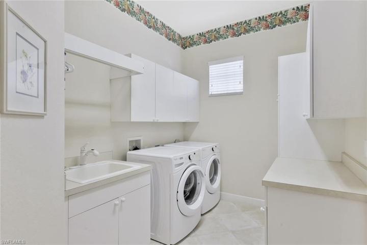 Additional cabinetry with drying bar over utility sink and beverage cooler in laundry room