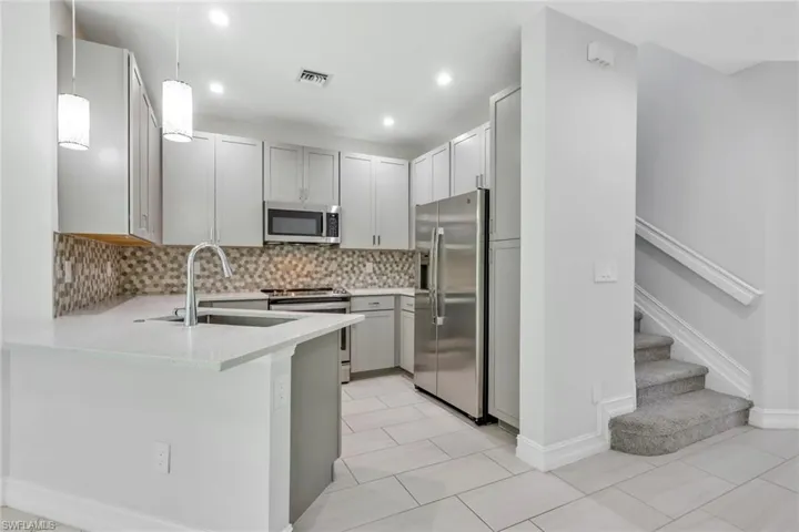 Kitchen featuring hanging light fixtures, stainless steel appliances, light stone counters, backsplash, and light tile patterned floors