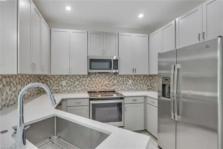 Kitchen featuring stainless steel appliances, tasteful backsplash, and light stone countertops