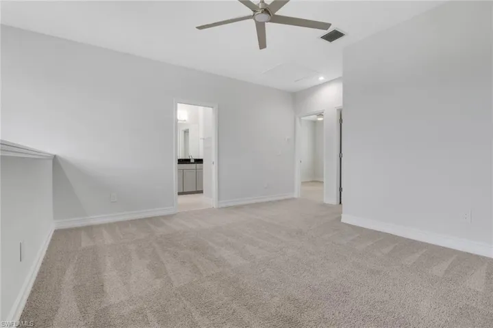 Empty room featuring light colored carpet, a ceiling fan, and attic access