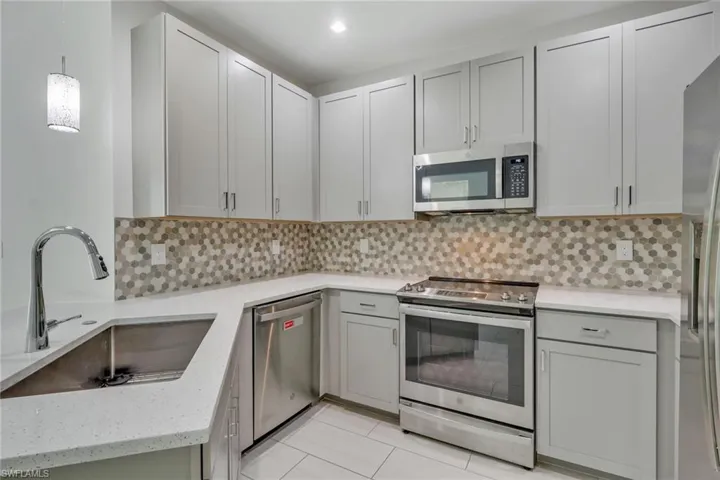 Kitchen featuring appliances with stainless steel finishes, decorative backsplash, pendant lighting, light stone counters, and gray cabinetry