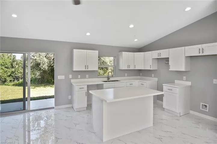 Kitchen featuring recessed lighting, vaulted ceiling, white cabinets, a center island, and light marble finish floors