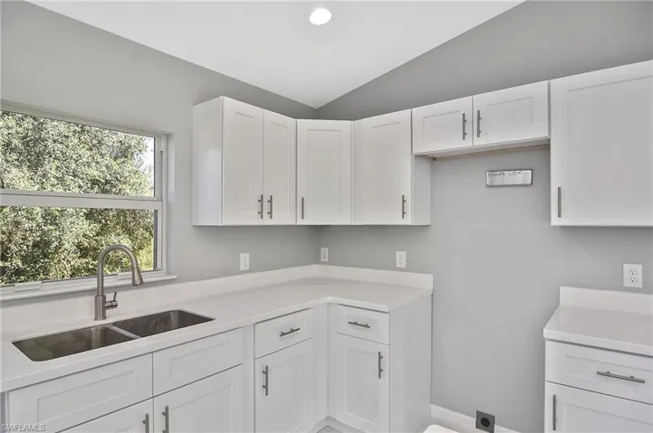 Kitchen featuring white cabinetry, vaulted ceiling, recessed lighting, and light stone counters