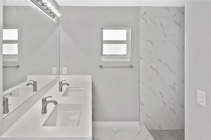 Bathroom featuring a marble finish shower, double vanity, and light marble finish flooring