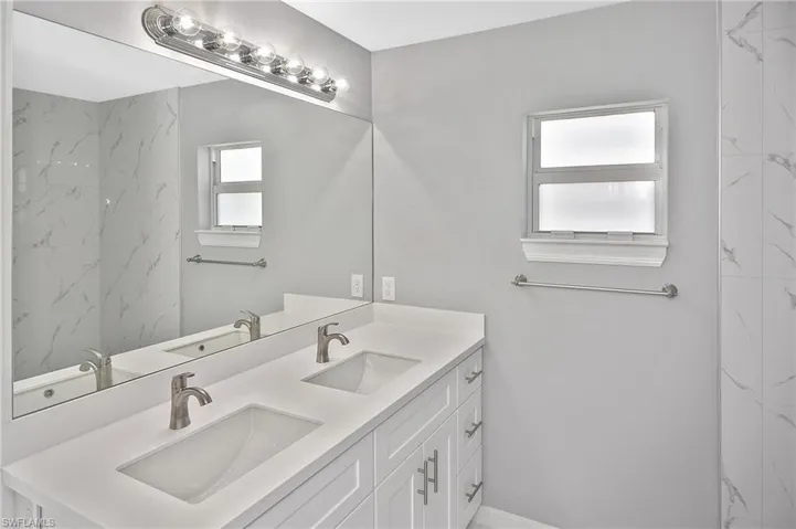 Bathroom with double vanity, a marble finish shower, and healthy amount of natural light