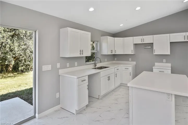 Kitchen featuring lofted ceiling, white cabinets, light marble finish flooring, recessed lighting, and a center island