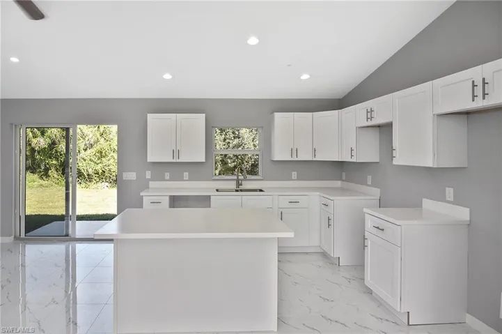 Kitchen featuring white cabinets, a kitchen island, recessed lighting, light countertops, and light marble finish flooring