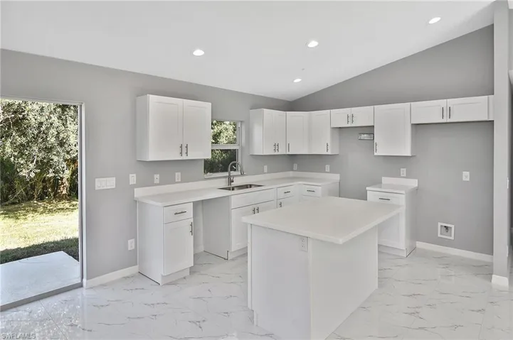 Kitchen with recessed lighting, white cabinets, light countertops, a kitchen island, and vaulted ceiling