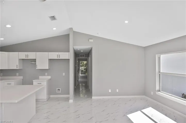 Kitchen featuring light countertops, light marble finish flooring, lofted ceiling, recessed lighting, and white cabinetry