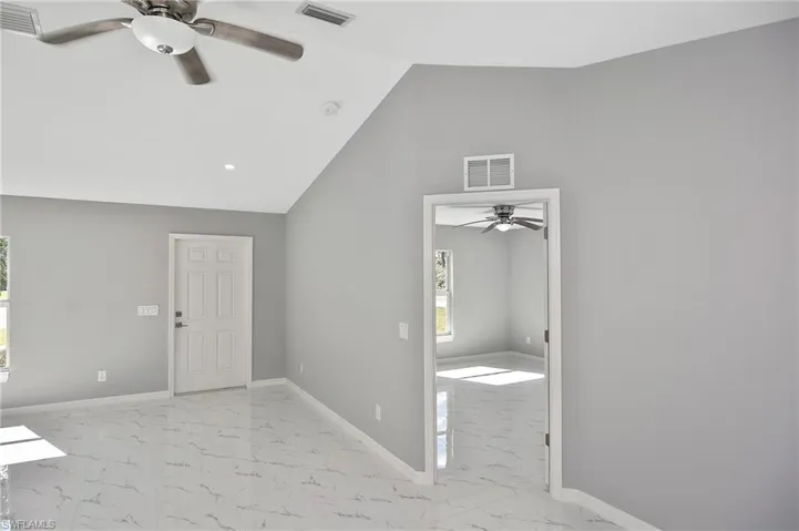 Empty room with a ceiling fan, light marble finish flooring, and lofted ceiling