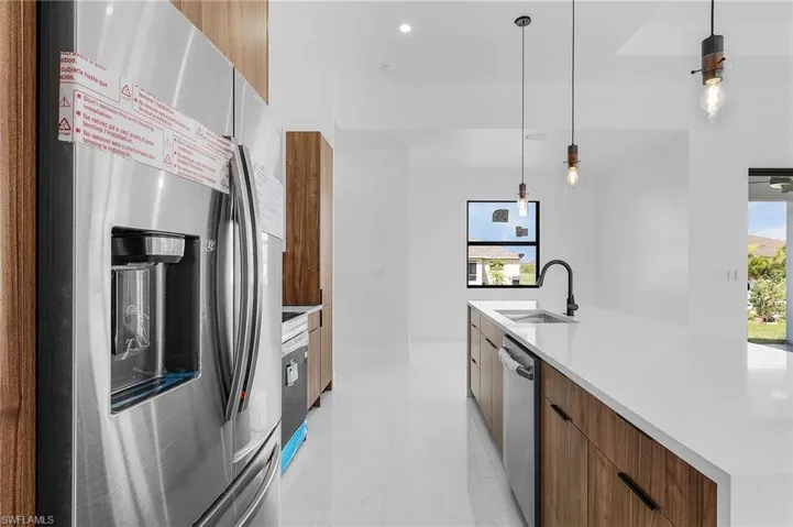 Kitchen featuring hanging light fixtures, stainless steel appliances, sink, and a center island with sink