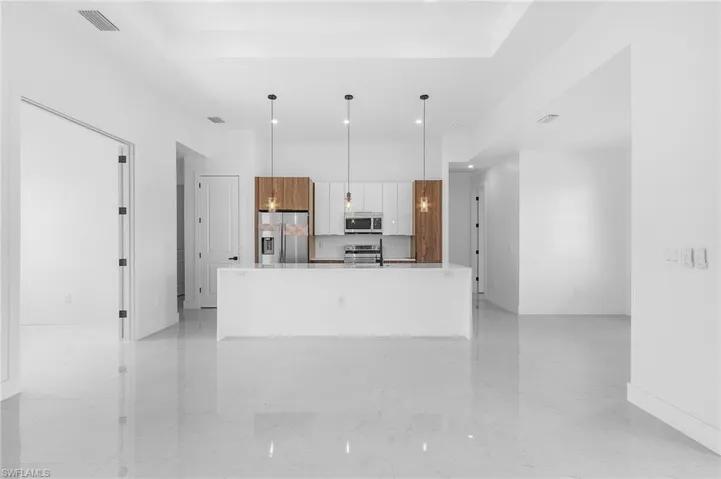 Kitchen with white cabinetry, stainless steel appliances, hanging light fixtures, a raised ceiling, and a center island with sink