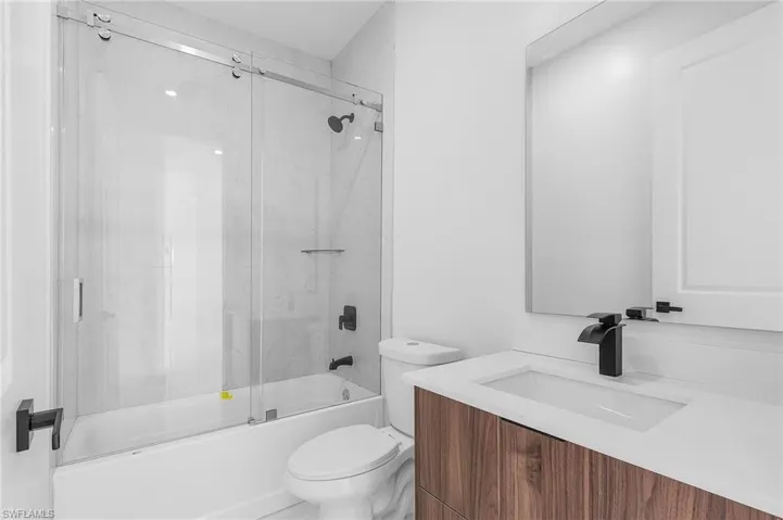 Full bathroom featuring toilet, combined bath / shower with glass door, and vanity