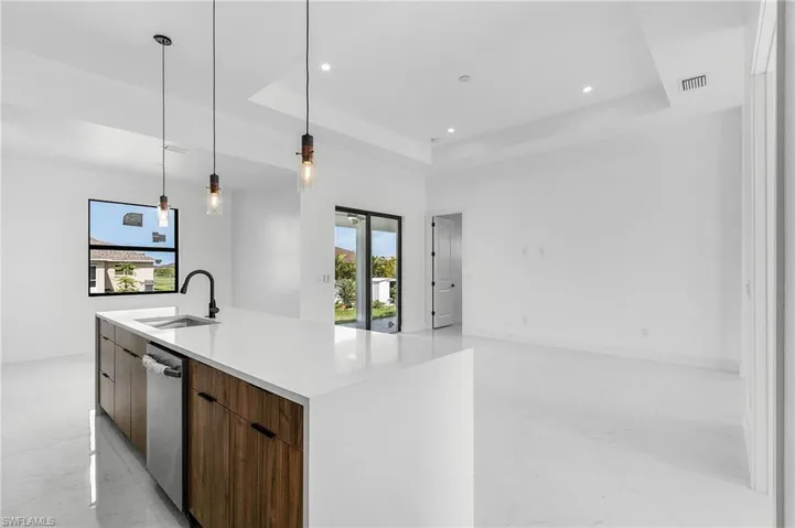 Kitchen with a raised ceiling, pendant lighting, a kitchen island with sink, stainless steel dishwasher, and sink