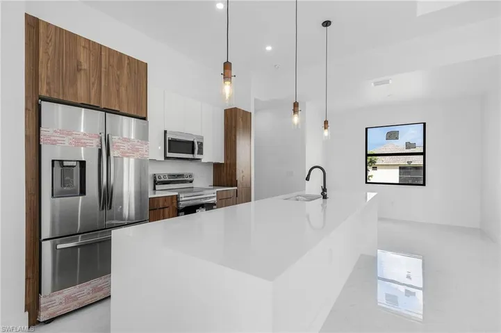 Kitchen with appliances with stainless steel finishes, decorative light fixtures, sink, and a center island with sink