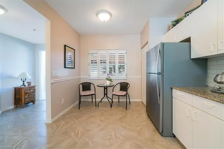 Kitchen featuring freestanding refrigerator, white cabinets, light stone counters, and decorative backsplash