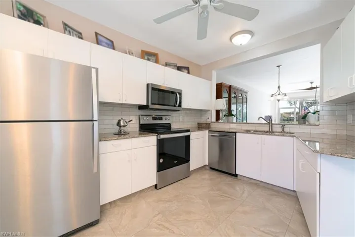 Kitchen with stainless steel appliances, light stone counters, hanging light fixtures, and white cabinetry
