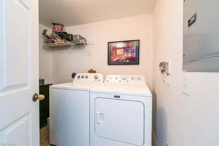 Laundry area with electric panel, separate washer and dryer, and a textured wall