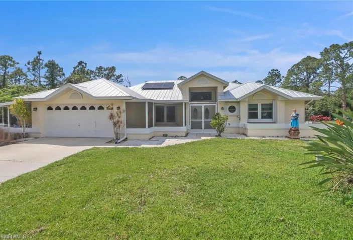 View of front of home featuring solar panels, driveway, a front lawn, a garage, and a metal roof