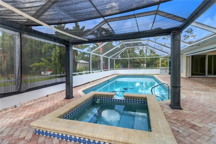 View of swimming pool featuring a patio area, a pool with connected hot tub, and glass enclosure