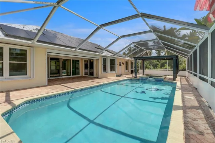View of pool with a patio area, a pool with connected hot tub, and glass enclosure
