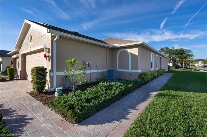View of side of property with a lawn, stucco siding, a garage, and decorative driveway