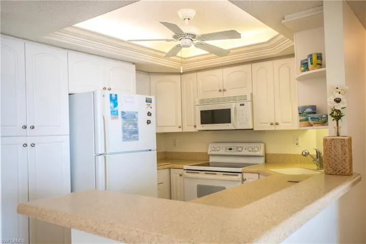 Kitchen with ornamental molding, a raised ceiling, sink, white cabinets, and white appliances