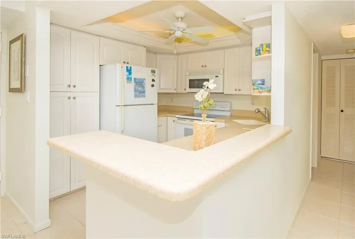 Kitchen with sink, kitchen peninsula, white appliances, a raised ceiling, and white cabinets