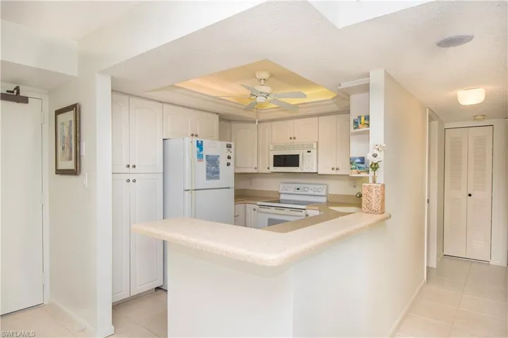 Kitchen with kitchen peninsula, ceiling fan, light tile patterned floors, a tray ceiling, and white appliances