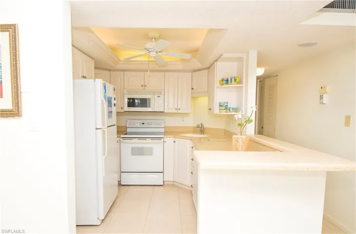 Kitchen with sink, kitchen peninsula, ceiling fan, white appliances, and a raised ceiling
